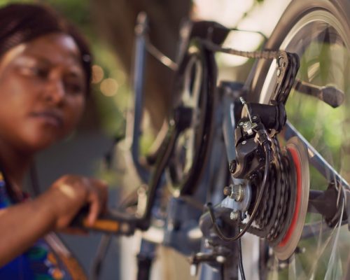 Detailed view of bicycle chain ring crank and barrel adjuster carefully examined and adjusted outside by african american lady. Close-up shot of black woman thoroughly inspecting bicycle cassette.